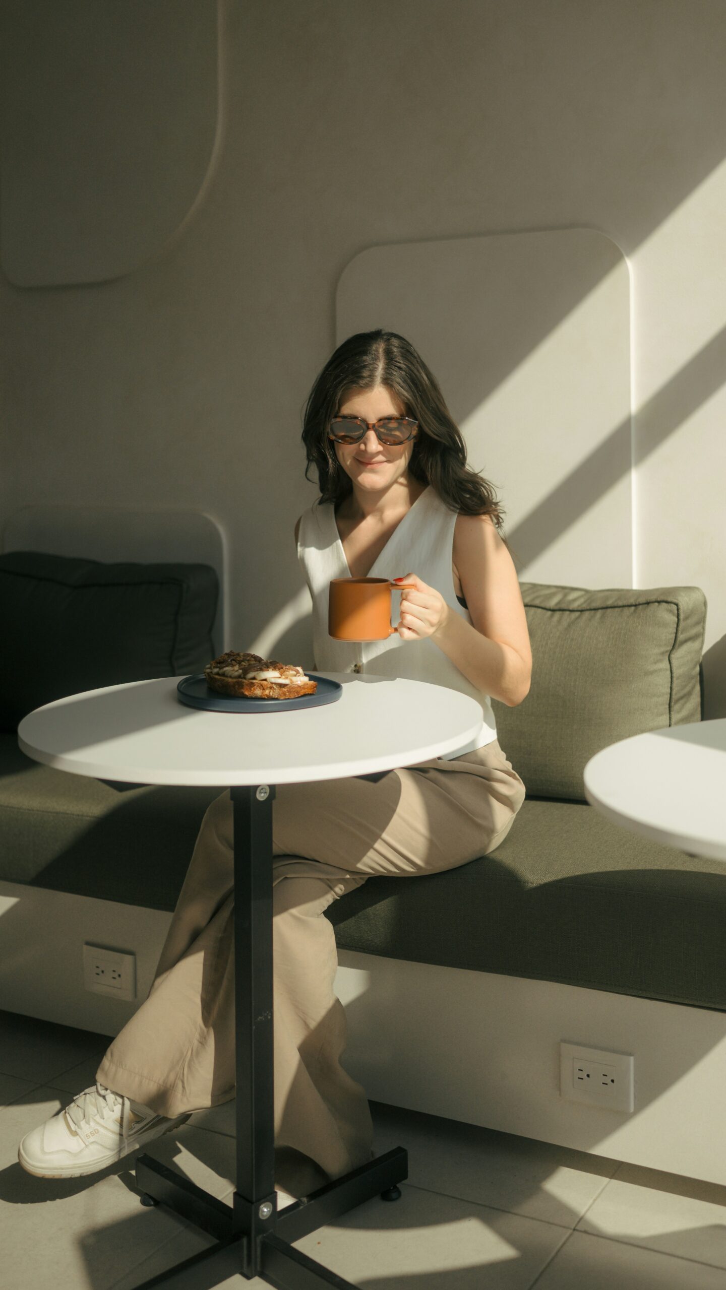 Happy woman sitting in a cozy modern kitchen drinking a cup of coffee and smiling looking at a tablet