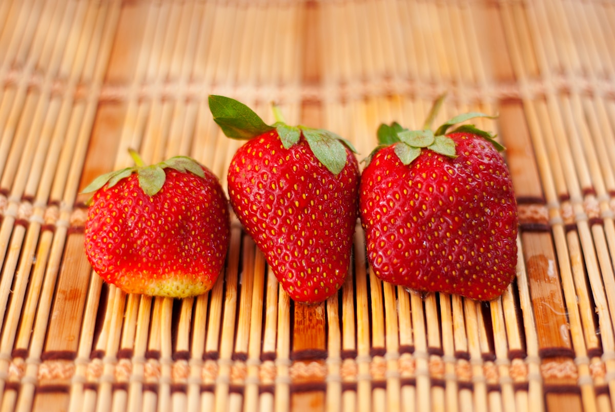 three strawberries sitting on top of a bamboo mat
